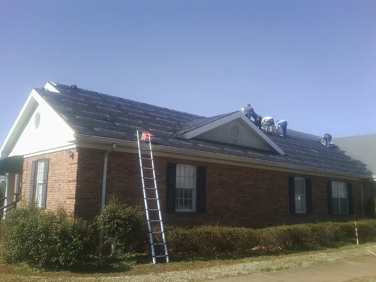 Crew tearing shingles off a brick ranch roof with a ladder set — Metal Roof Repair work by our crew in Bettsville