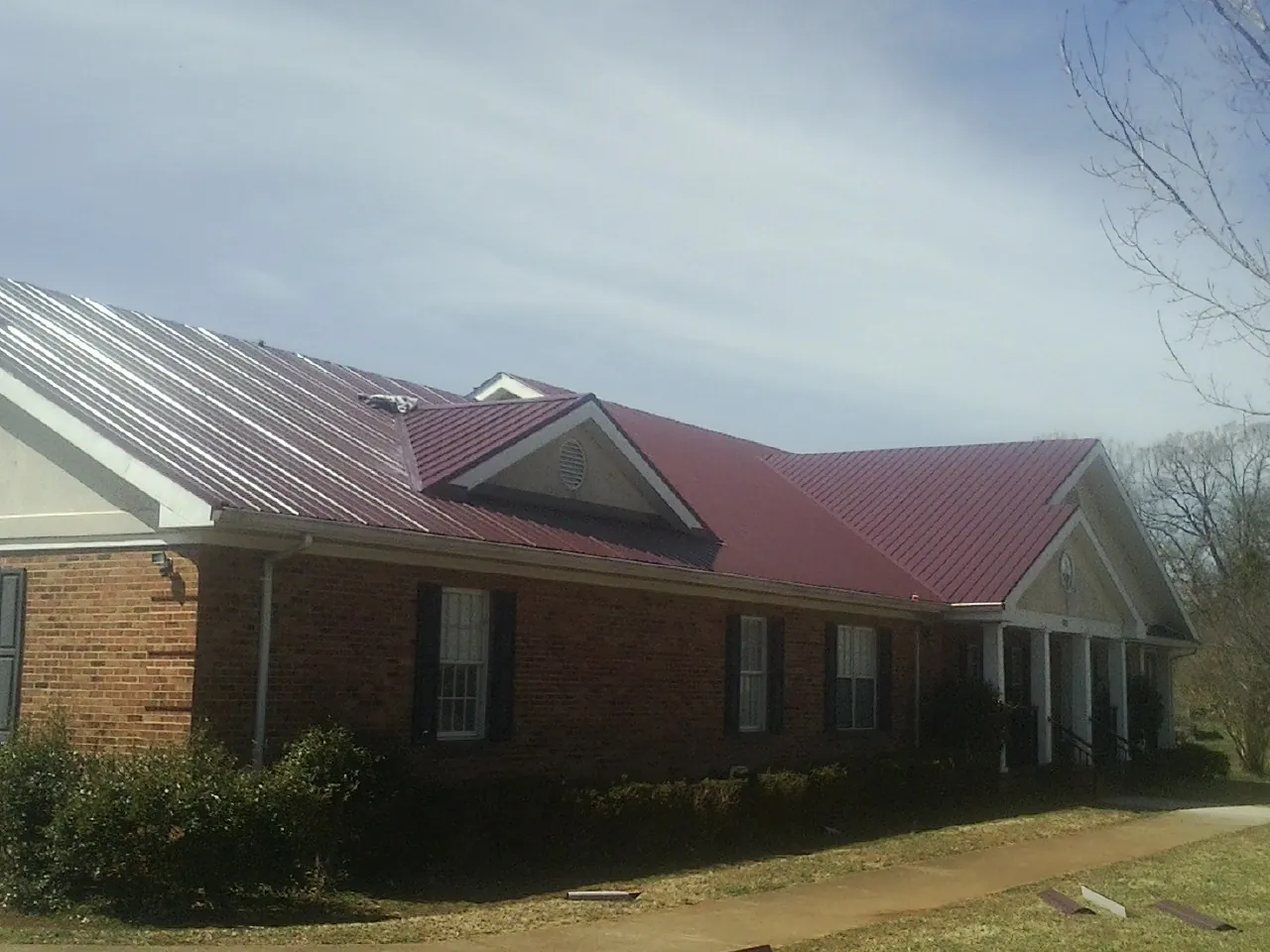 Red metal roof with gabled entries on a long brick building, from a Hail Damage Roof Repair job in Bettsville