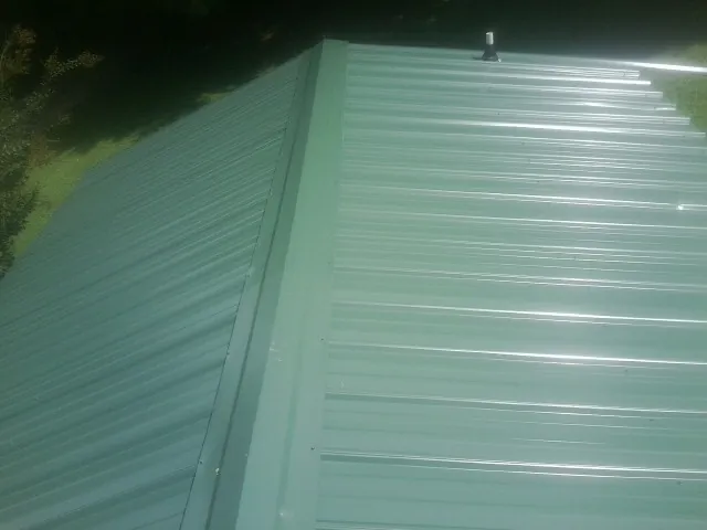 New green metal panels meeting at the ridge of a roof — Flat Roof Repair work by our crew in Bettsville