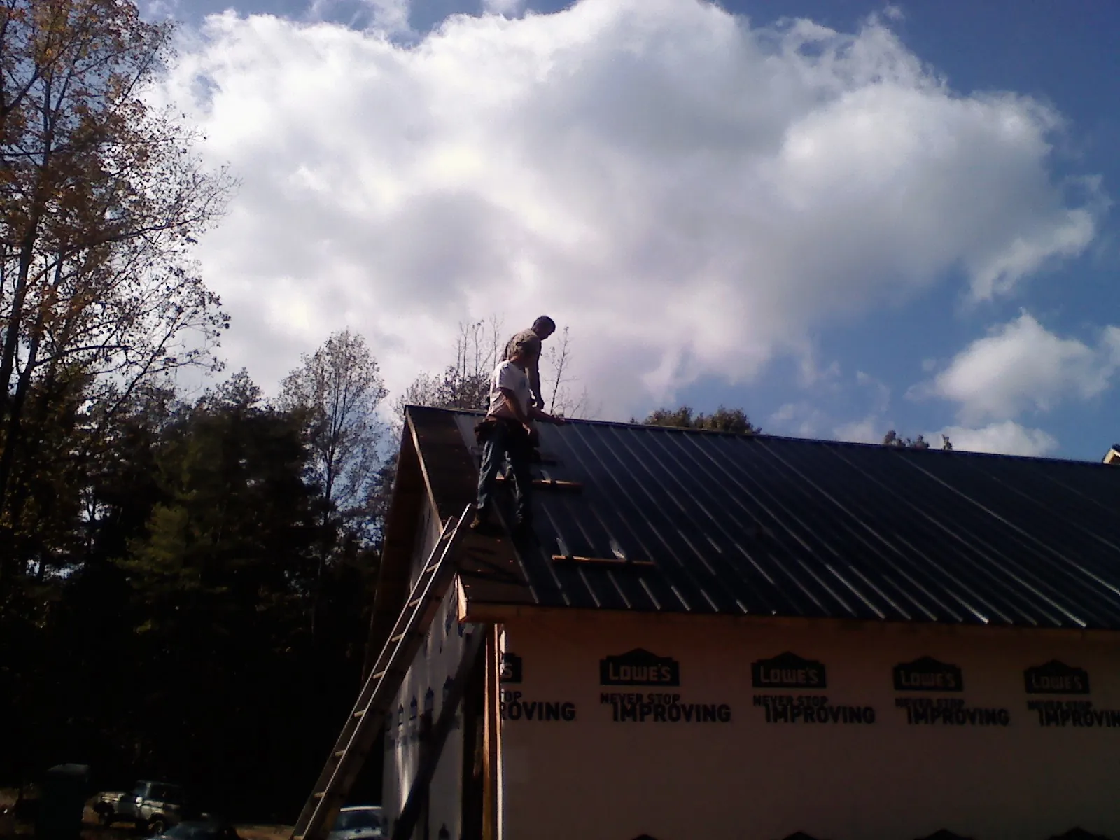 Roofer fastening dark metal panels high against a cloudy sky, from a Roof Inspection job in Bettsville