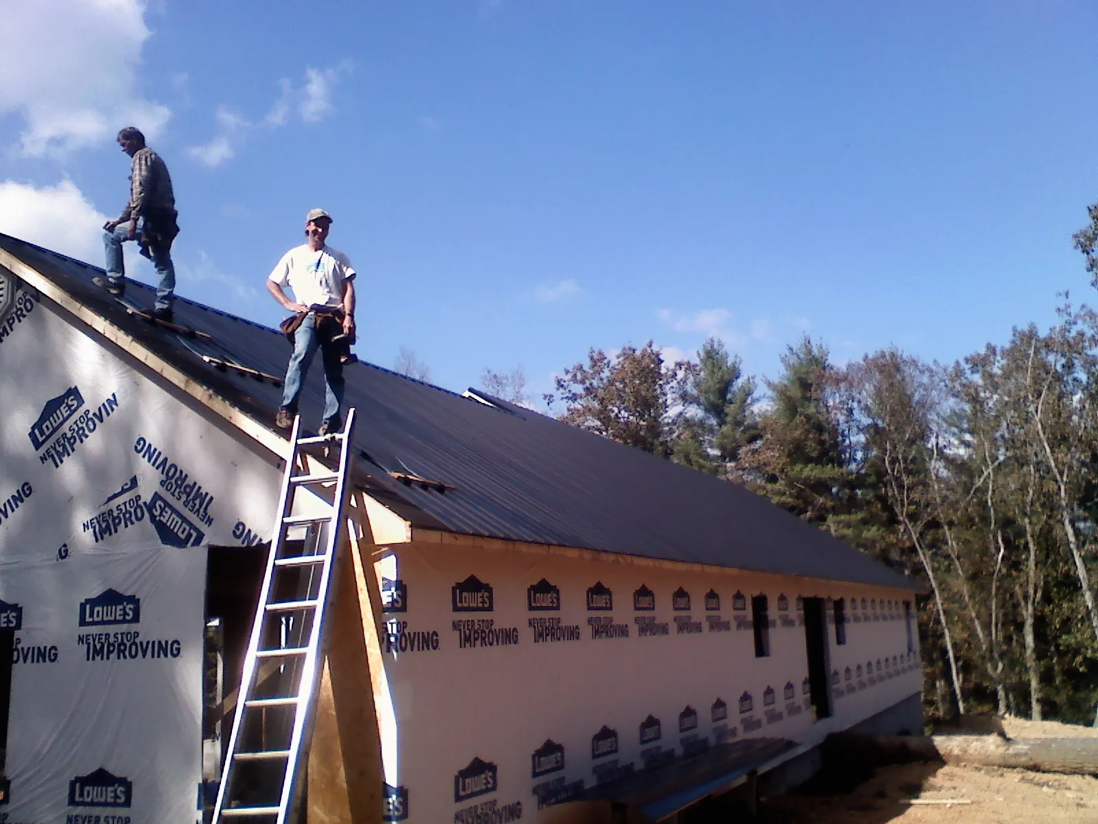 Two roofers standing on a long dark metal roof over a wrapped building in Bettsville