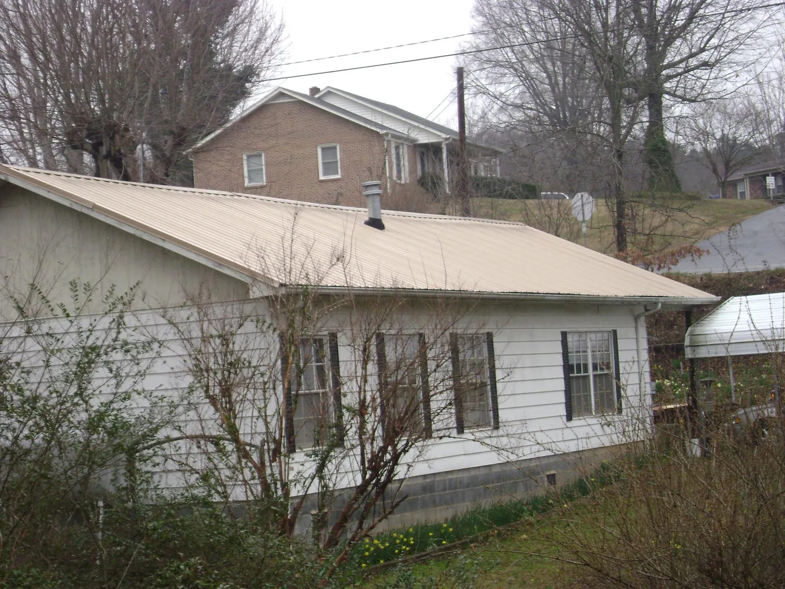 Tan metal roof on a white sided house set into a hillside — Commercial Roofing by Roofing Brothers in Bettsville