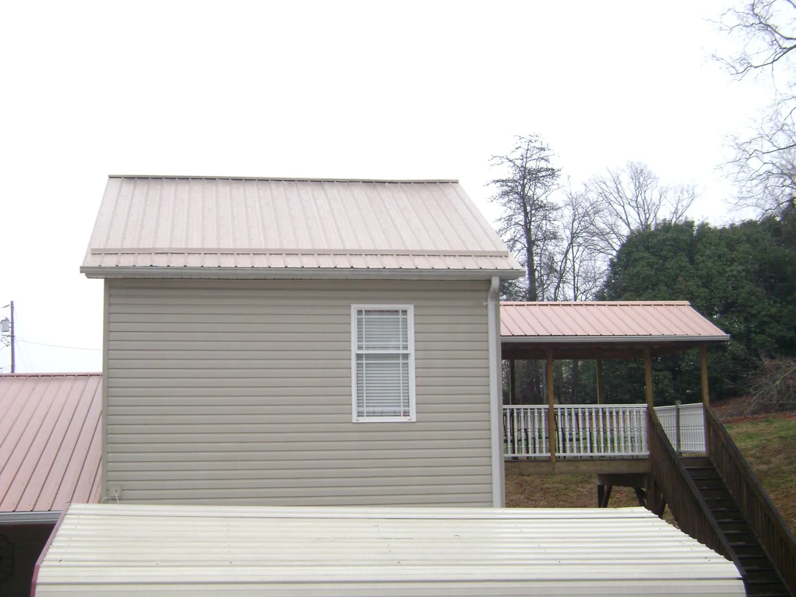 Tan metal roofs on a two story addition and attached porch, from a Roof Replacement job in Bettsville